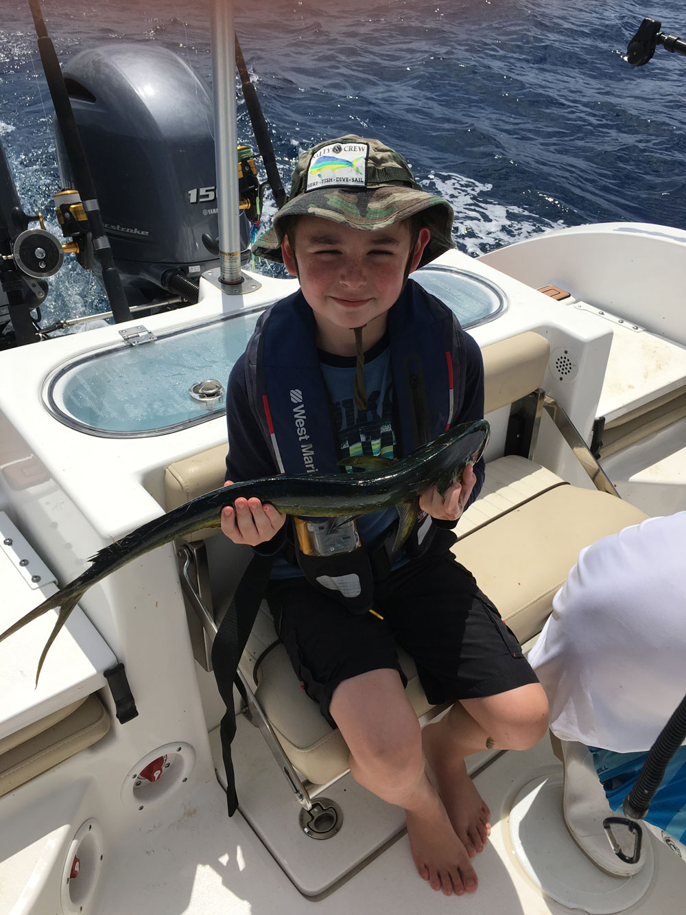 Boy sitting on the boat with dark colored fish in hands
