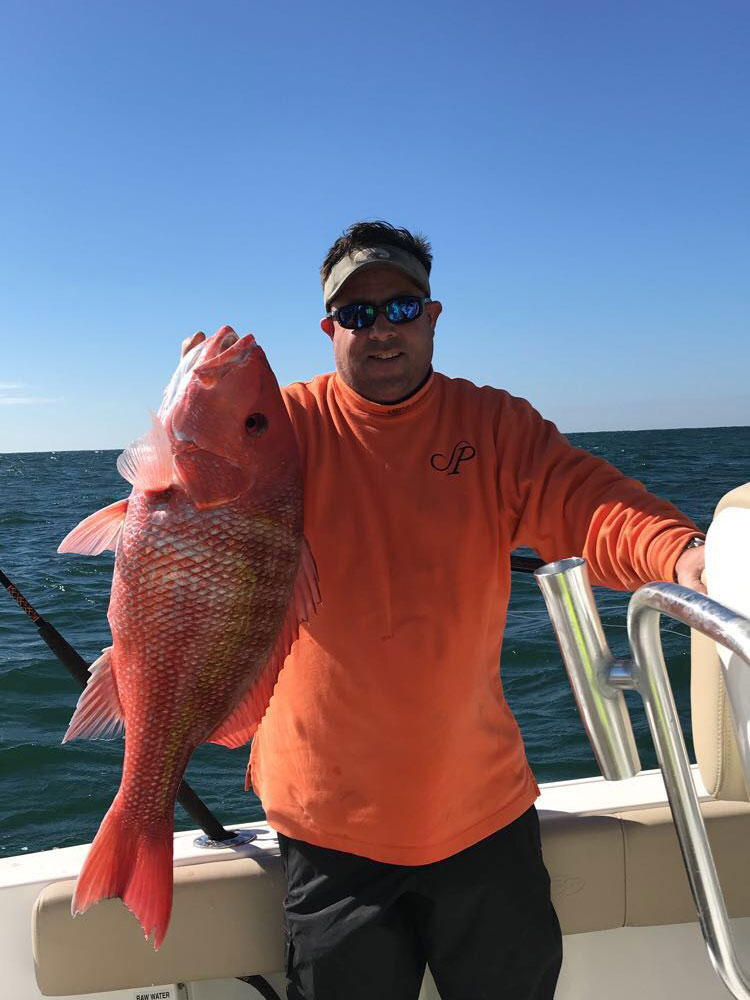 Chris Worth holding a red fish in right hand standing on the boat
