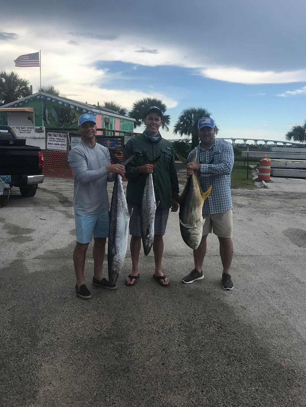 three men each holding one fish standing next to each other outdoors