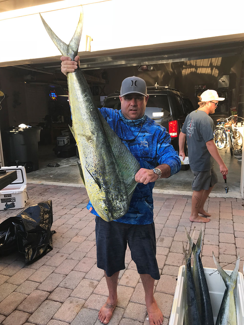 Chris Wroth holding large mahi fish by tail and by top fin in a driveway