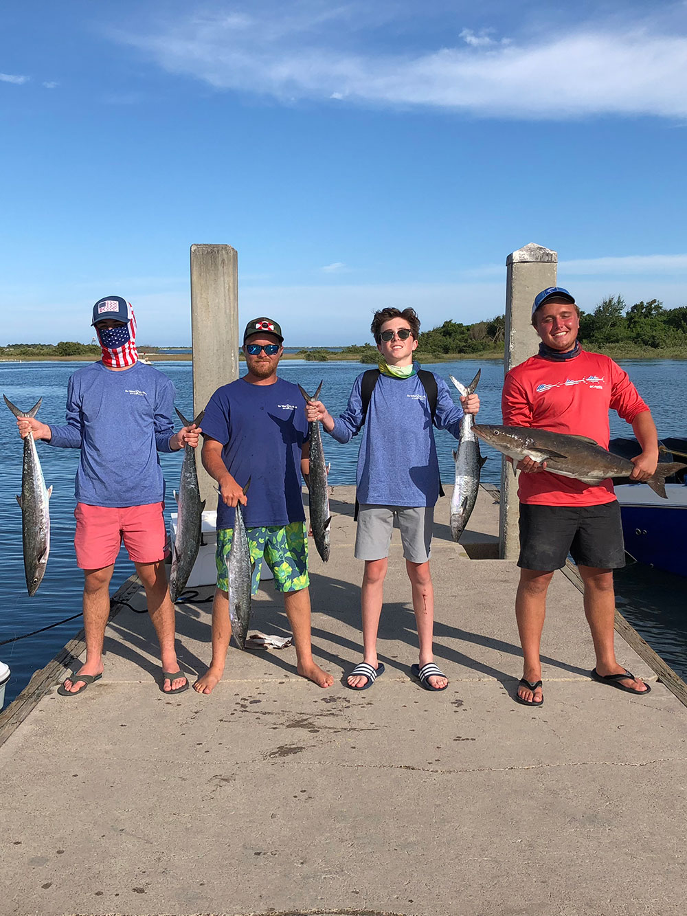 group of 4 men each holding fish while standing on a dock